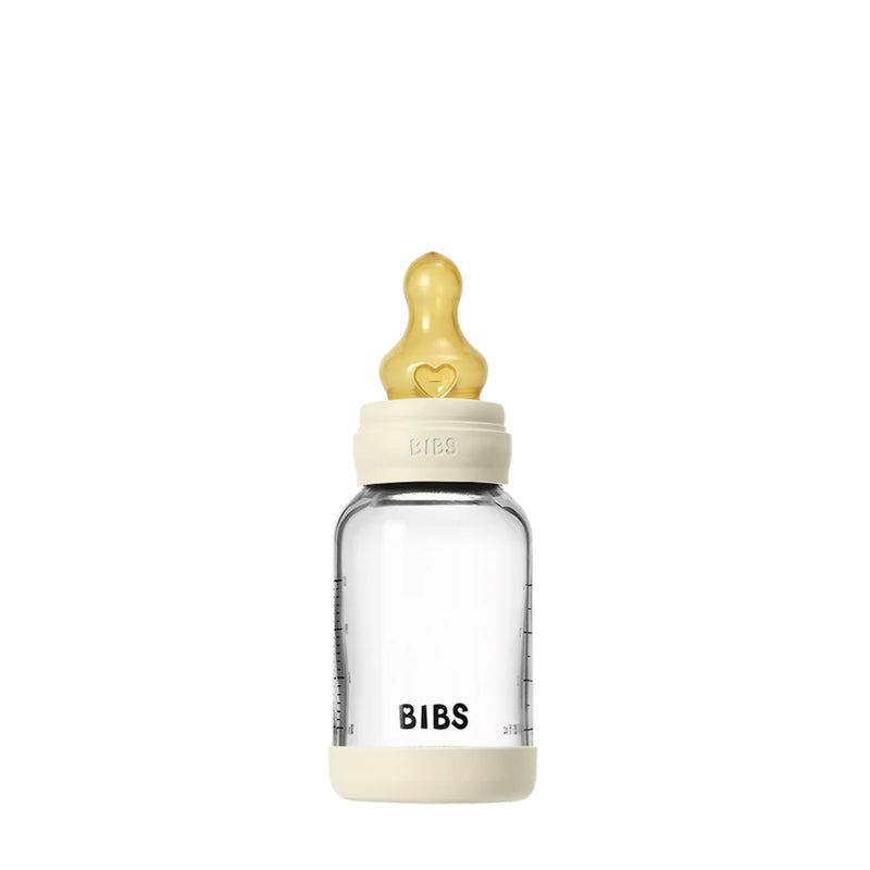 Clear baby bottle with beige cap and heart-shaped nipple on a white background
