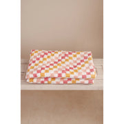 Folded checkered blanket with pink, yellow, and white pattern on a beige surface.