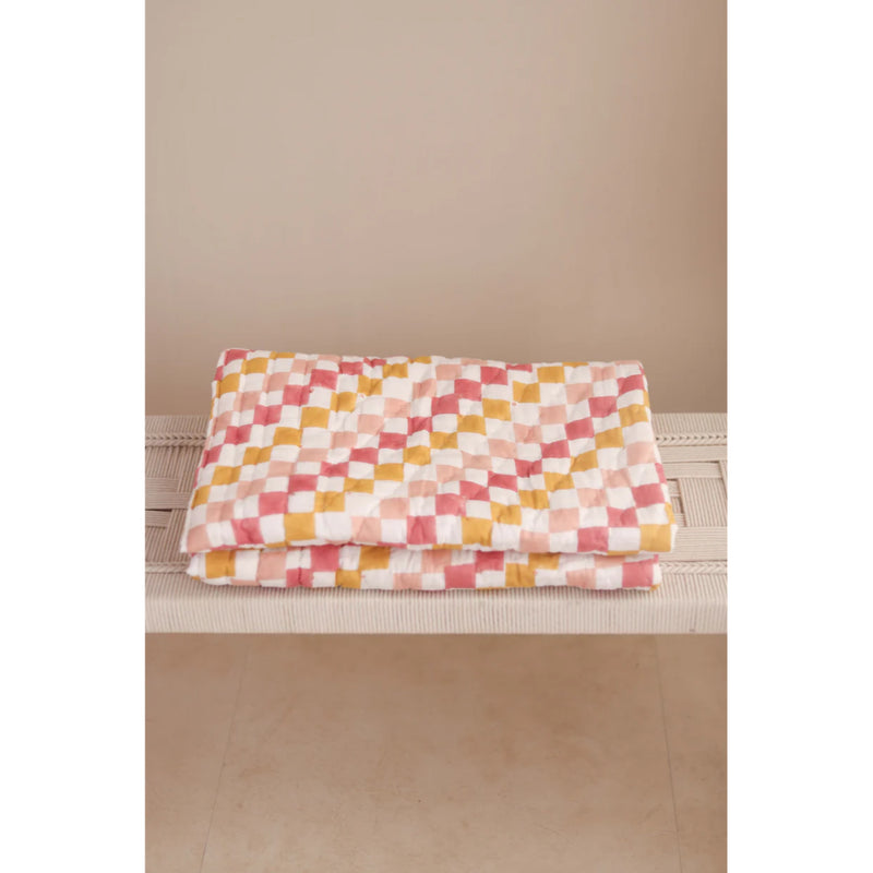 Folded checkered blanket with pink, yellow, and white pattern on a beige surface.