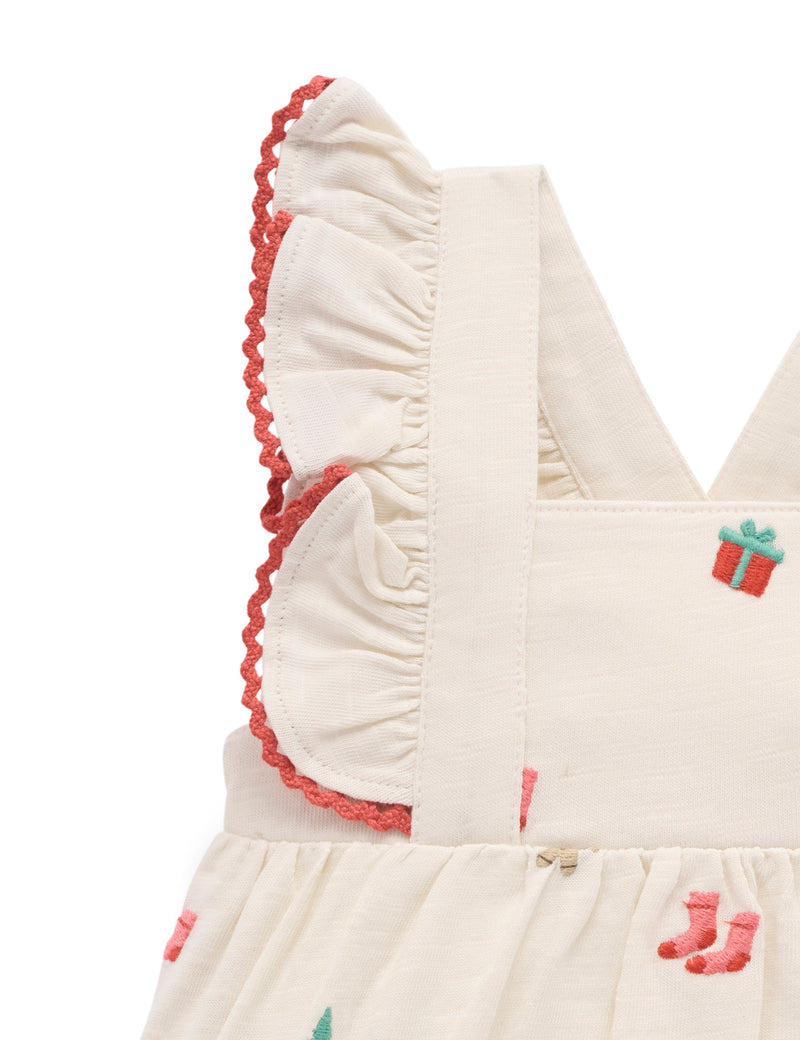 Close-up of a baby dress with ruffled details and embroidered designs on a white background